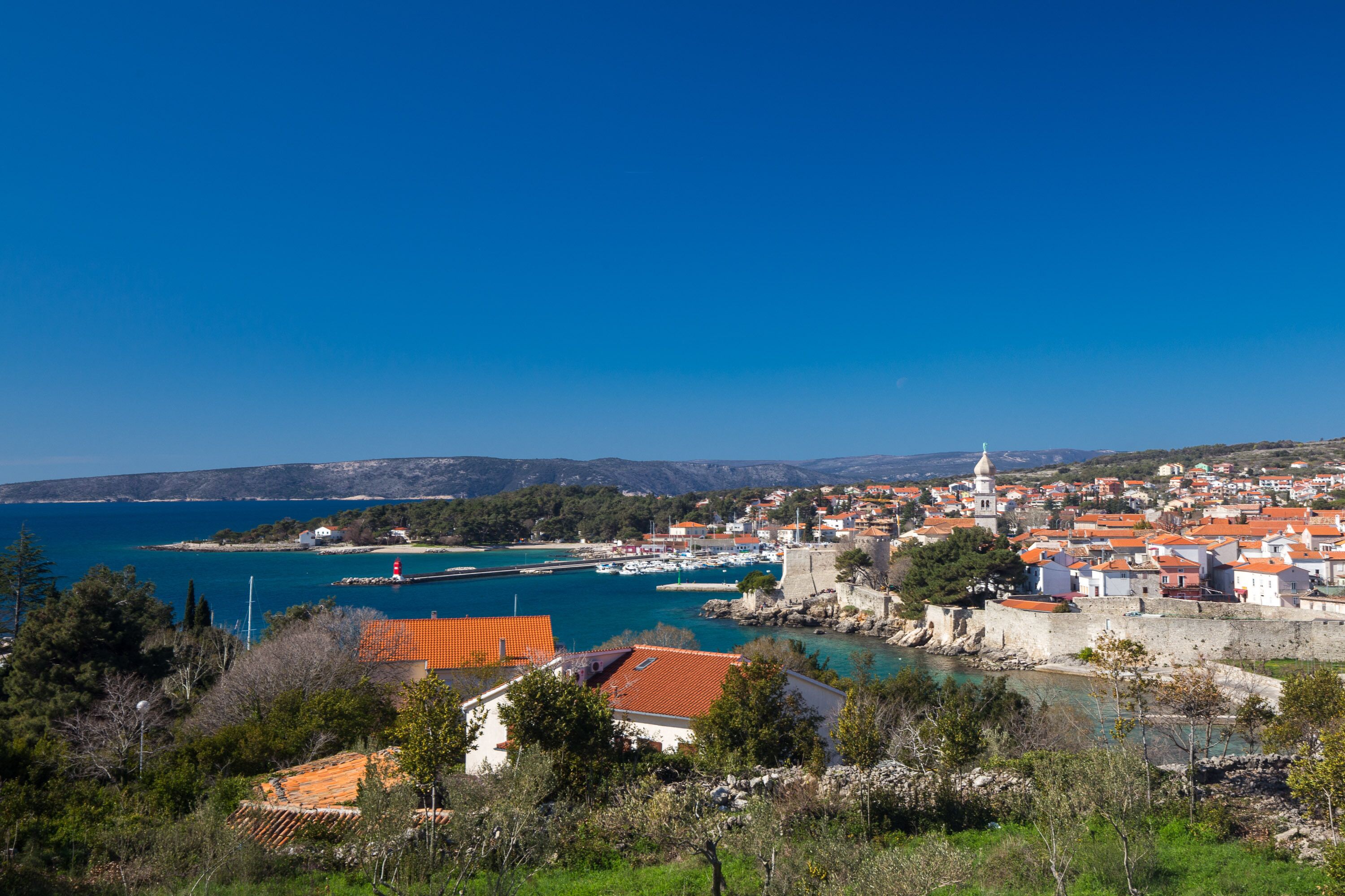 A coastal town with a historic fortification, a harbor with boats, and a clear blue sky.