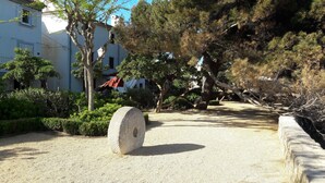Un sendero de grava serpentea por un área ajardinada con árboles y una estructura de piedra.