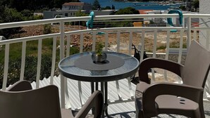 Un balcón con una mesa redonda y dos sillas, con vistas a la costa, casas y una masa de agua.