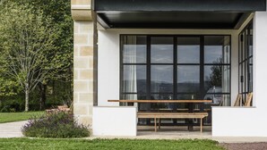 Un edificio moderno con ventanas amplias, un banco de madera y un muro de piedra.