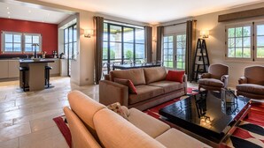 Un salón amplio con un ventanal grande, una zona de cocina y un área de descanso con sofá y sillones.