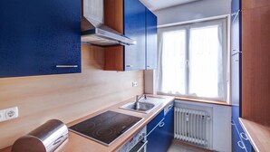 A compact kitchen with a stove, sink, and built-in oven. There is a window providing natural light and a radiator below the window.