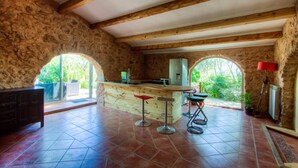 Una cucina rustica con pareti in pietra, travi in legno, un angolo bar con sgabelli e ampie finestre ad arco.