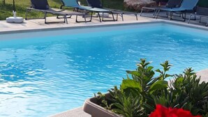 A swimming pool with lounge chairs and umbrellas, surrounded by greenery and red flowers. - Casa di campagna per famiglie (Vodnjan)