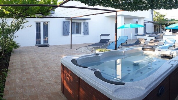 A hot tub in a backyard with a patio area, outdoor seating, and a white building in the background. - Casa di campagna per famiglie (Vodnjan)