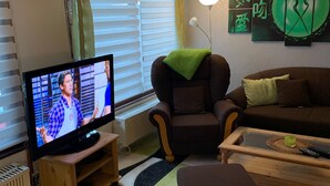 Una sala de estar con televisión, un sillón marrón, un sofá marrón, una mesa de centro y una lámpara de pie.