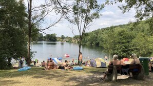 Un camping junto al lago con tiendas de campaña, piscinas inflables y gente relajándose junto al agua.