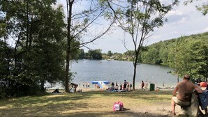 Un parque junto al lago con árboles, un área de picnic y gente descansando junto al agua.