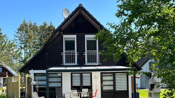 Una casa de dos pisos con garaje, un patio con mobiliario exterior y un césped bien cuidado.
