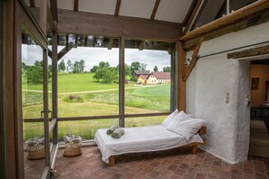 Un dormitorio con un ventanal grande, una cama y vistas a una casa y campos.