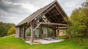 A rustic wooden cabin with a sloped roof, large windows, and a patio area with outdoor seating.