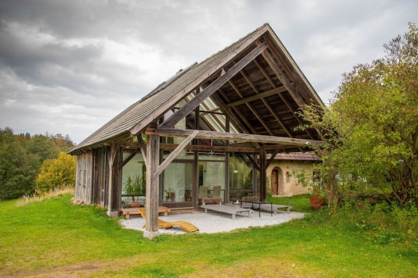 Una cabaña de madera rústica con techo inclinado, ventanas amplias y un patio con mobiliario exterior.