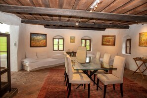 Un comedor con una mesa y sillas de vidrio, cojines blancos y cuadros en las paredes.