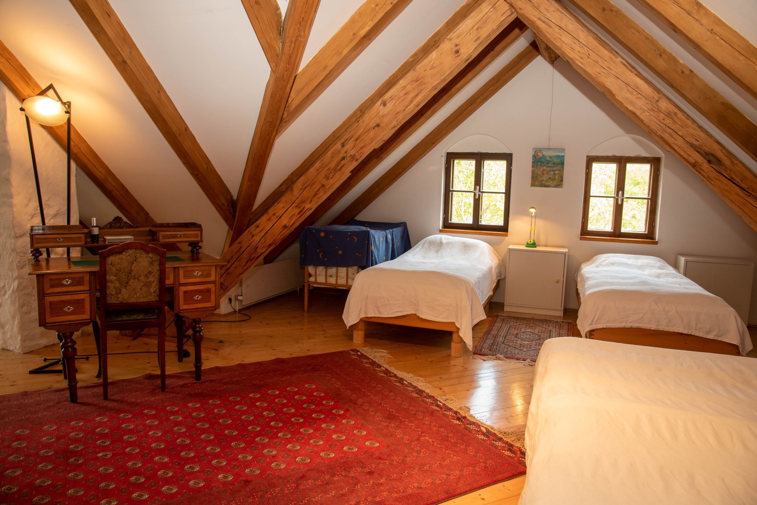 A cozy attic bedroom with wooden beams, two beds, a desk, and a chair.