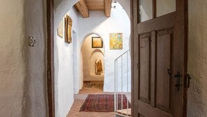 A hallway with a wooden door, white walls, and a tiled floor leading to a room with a red carpet.