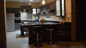 Una cocina moderna con una isla central, taburetes de bar, electrodomésticos de acero inoxidable e iluminación colgante.