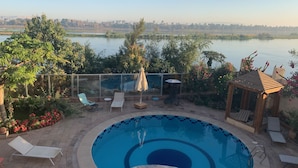 Zona de piscina con sillas de descanso y una pérgola, rodeada por un jardín con plantas en flor.