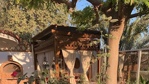 Un jardín con flores rojas, una pérgola de madera y un muro de ladrillo.