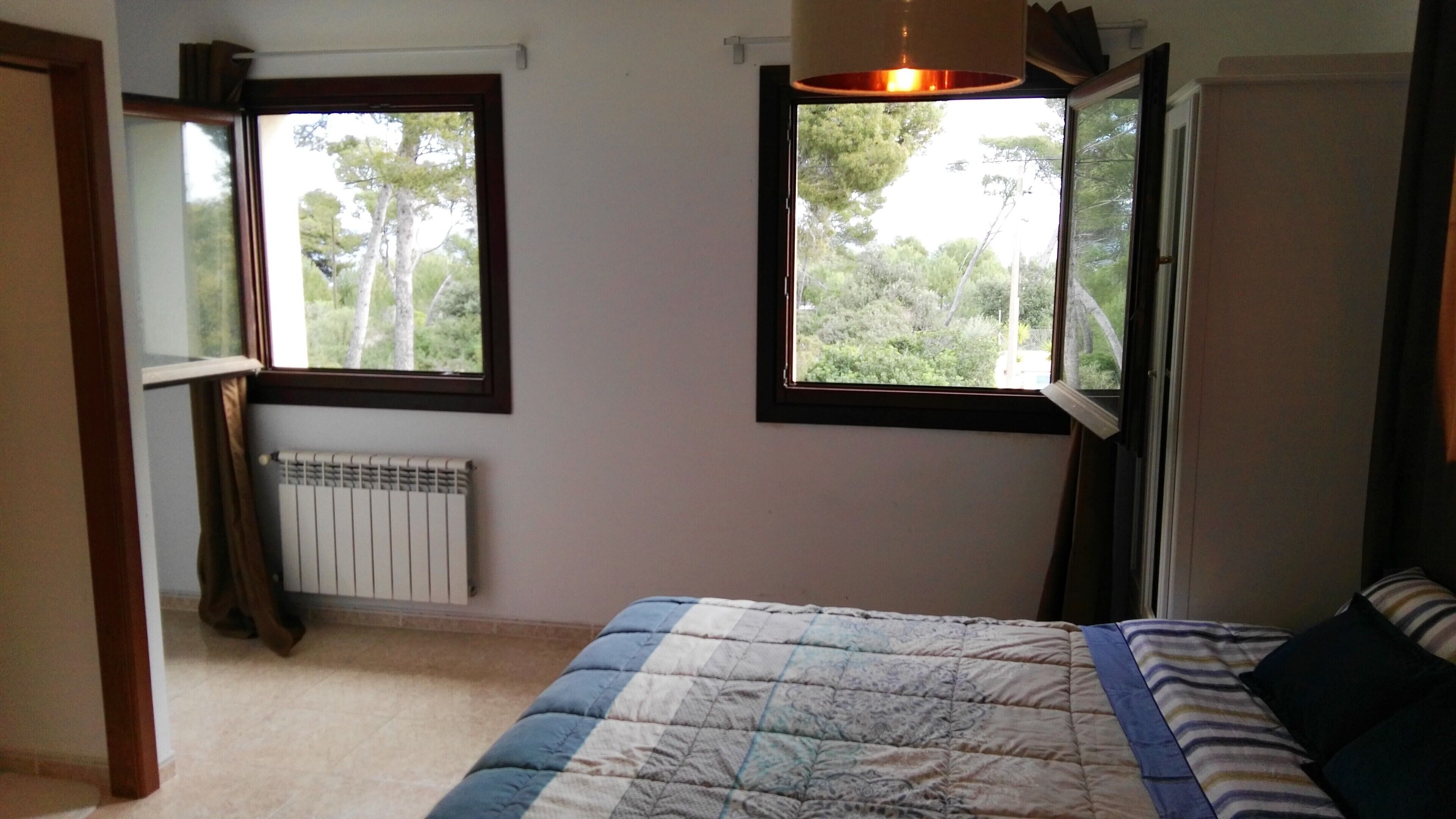 Un dormitorio con cama, dos ventanas, un radiador y una lámpara colgante.
