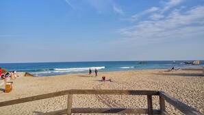 Uma praia com grade de madeira, areal arenoso e algumas pessoas caminhando e sentadas.