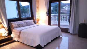 Quarto com cama, mesa de cabeceira, abajur e vista para o exterior.
