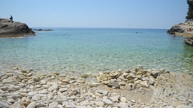 A rocky beach with clear shallow water, a distant view of the sea, and a few people in the background. - Holiday home in Pula,2 km from the amphitheater,family-friendly,quietly,WIFI (Pula)