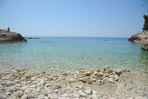 A rocky beach with clear shallow water, a distant view of the sea, and a few people in the background. - Holiday home in Pula,2 km from the amphitheater,family-friendly,quietly,WIFI (Pula)