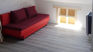 Une pièce avec un canapé rouge, une lucarne et un plancher en bois.