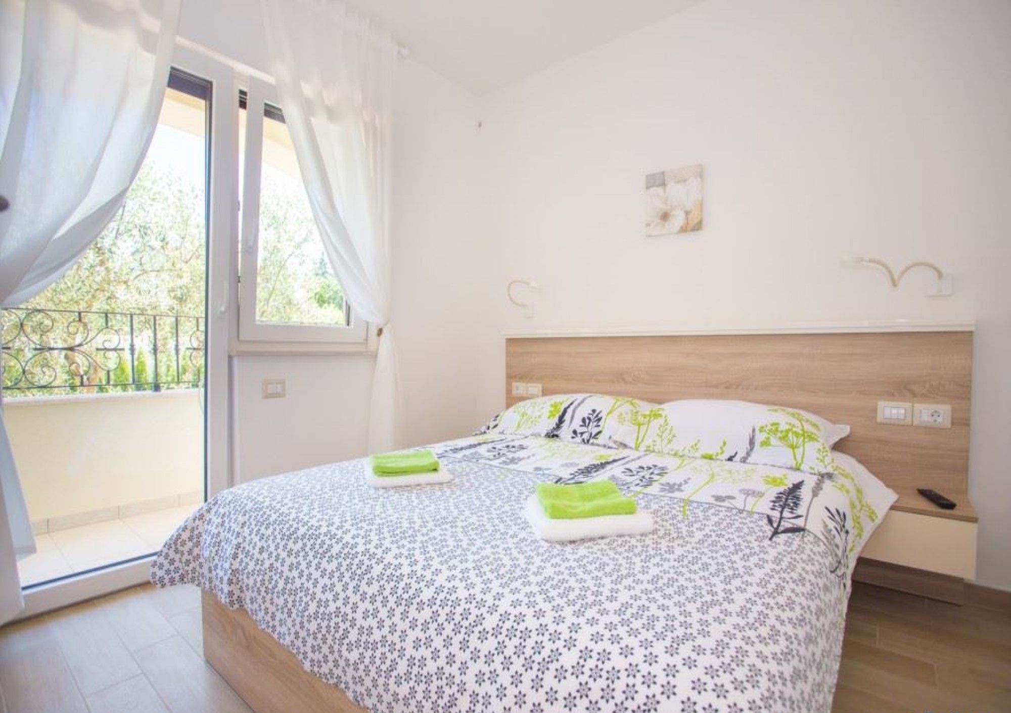 Una camera da letto con un letto, un comodino, una finestra con tende e un balcone.
