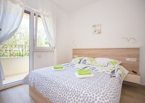 Un dormitorio con cama, mesita de noche, ventana con cortinas y balcón.
