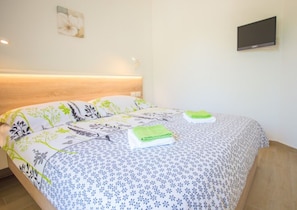 Una cama bien hecha con ropa de cama floral, un televisor de pantalla plana en la pared y un cabecero de madera.