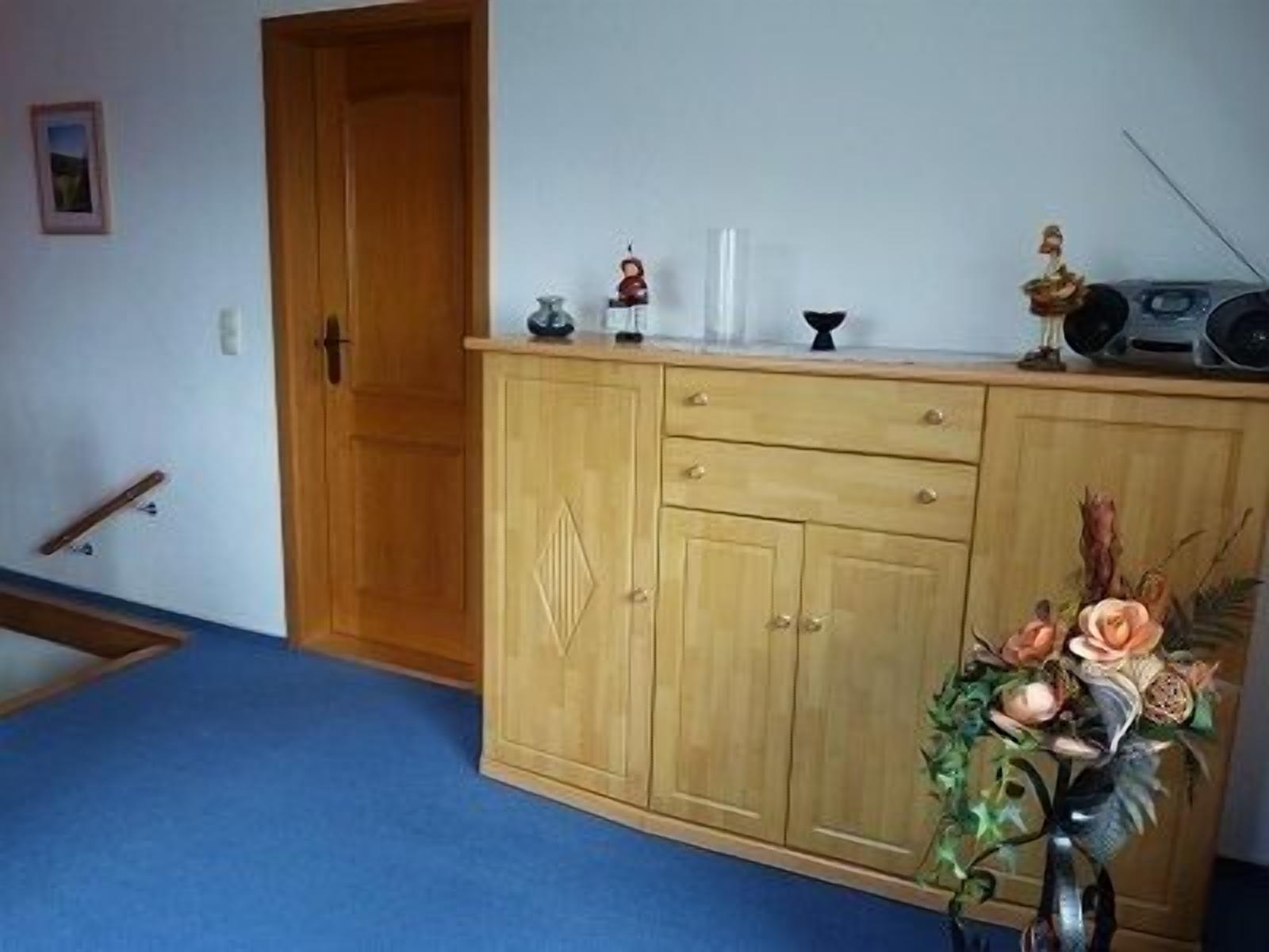 A room with a wooden cabinet, a blue carpet, and a decorative vase with flowers.