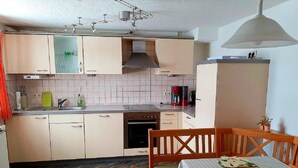 A compact kitchen with light-colored cabinets, a built-in oven, and a dining area with a wooden table and chairs.