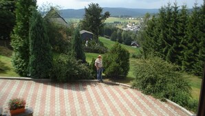 A man standing on a paved patio with a view of a rural landscape, including houses and trees.