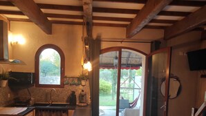 A rustic kitchen with a stone wall, wooden beams, a sink, and a window overlooking a garden. - Gite les Cypres in Velleron, on the edge of Sorgues (Velleron)