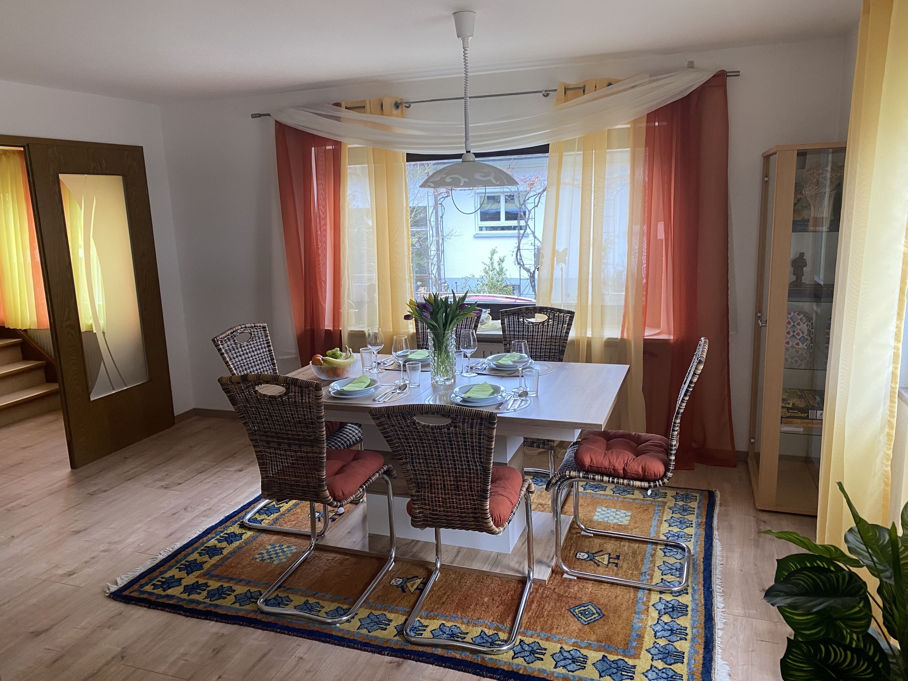 Un comedor con una mesa preparada para cuatro personas, rodeado de sillas de mimbre con cojines.