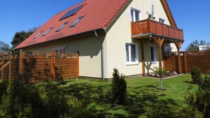 Uma casa de dois andares com telhado de telhas vermelhas, varanda e painéis solares.