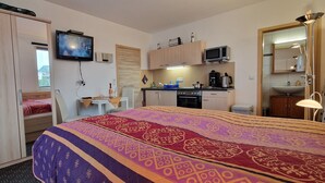 Quarto de hotel com cama, televisão, cozinha compacta e banheiro.
