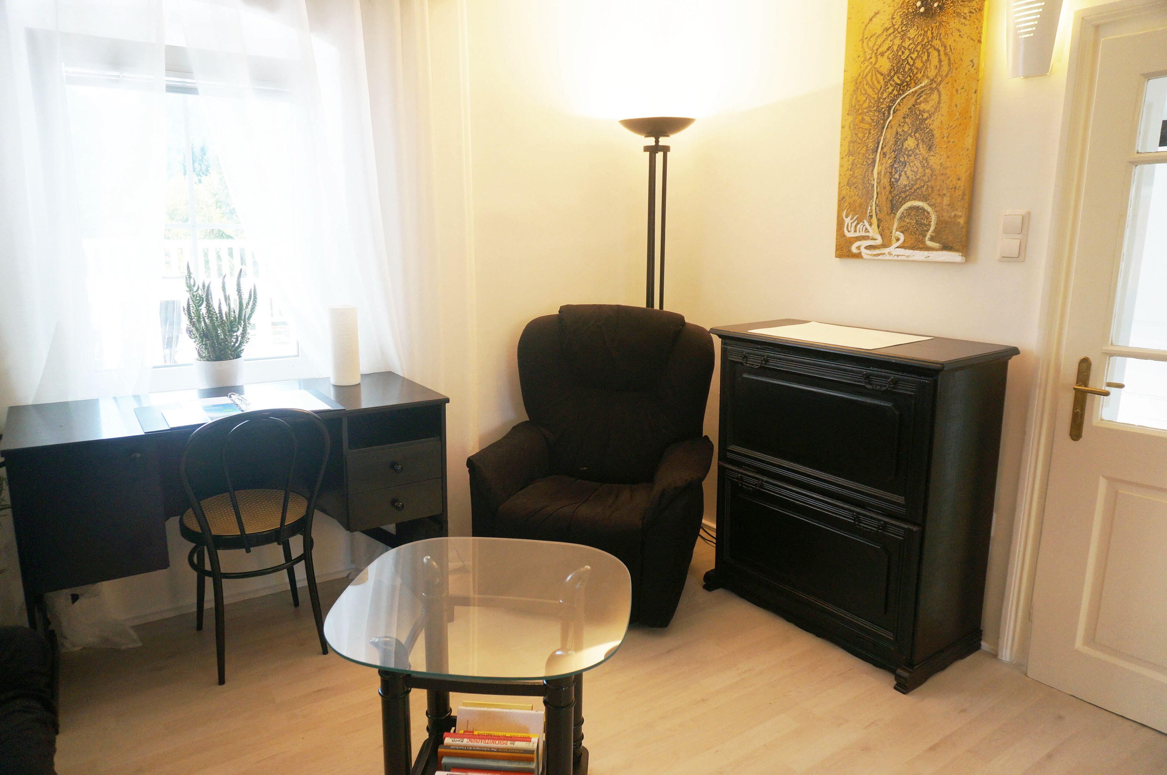 A room with a desk, a chair, a small table, a lamp, and a cabinet.