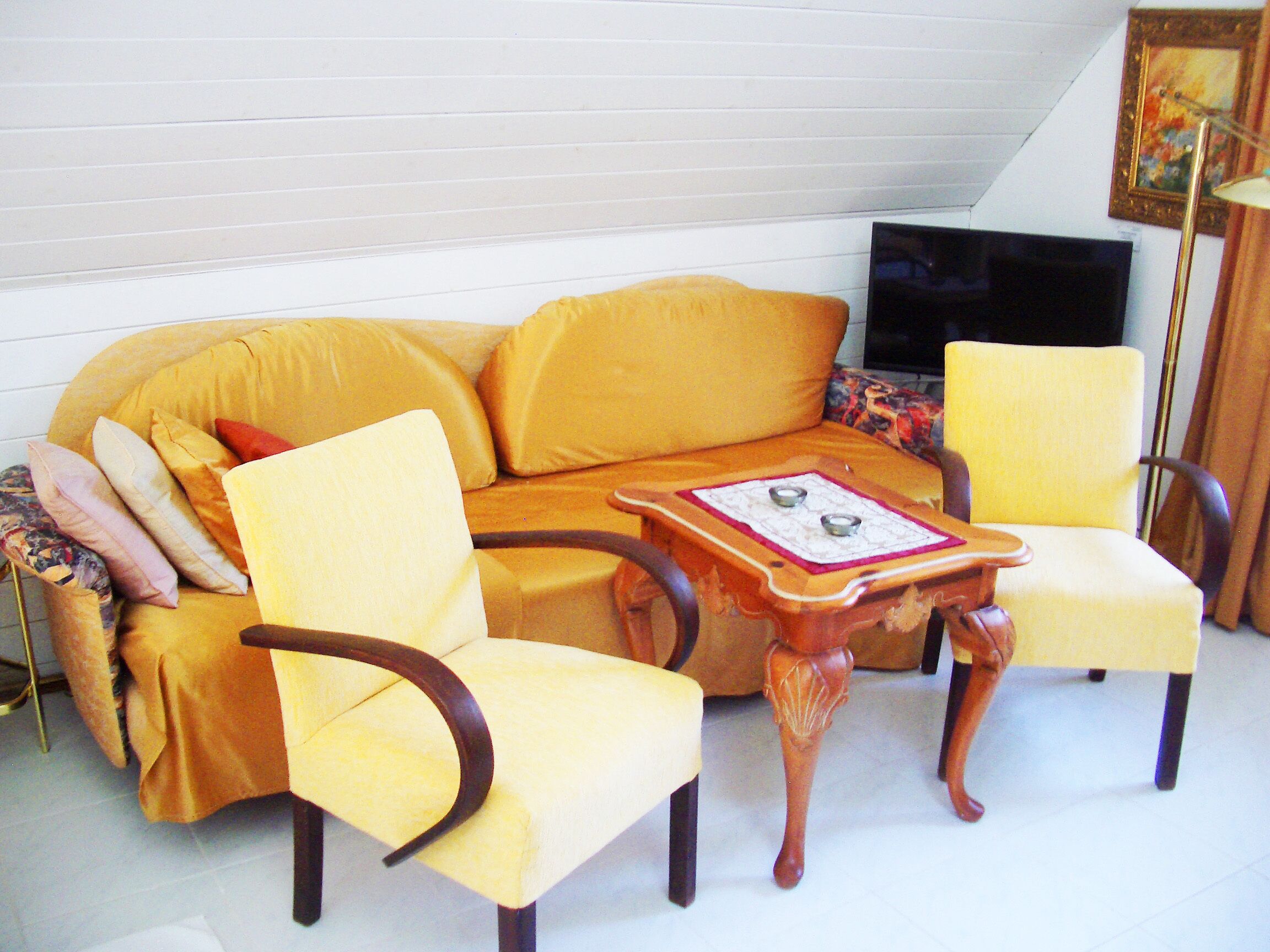 A yellow sofa with matching armchairs and a wooden coffee table with candle holders.