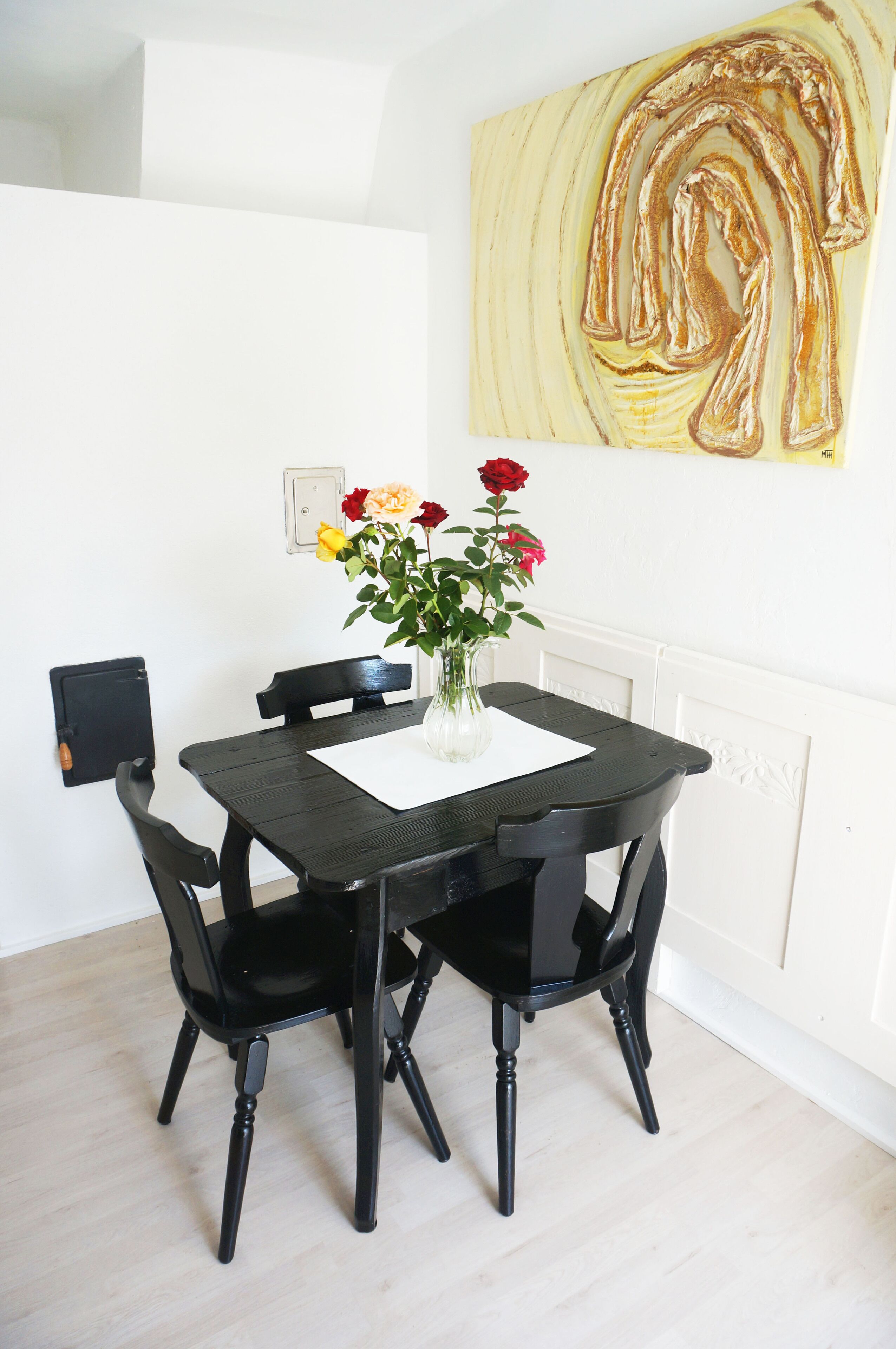 Una mesa de comedor con un florero, sillas negras y un interruptor de luz en la pared.