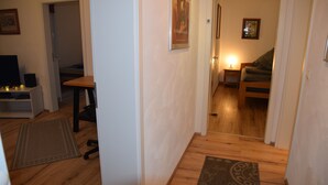 Un couloir avec un plancher en bois, un tapis, un bureau avec un ordinateur et, au fond, un lit.