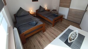 Une chambre à coucher avec deux lits en bois, des lampes de chevet, une petite table ornée d’un objet décoratif et une vue sur l’extérieur.
