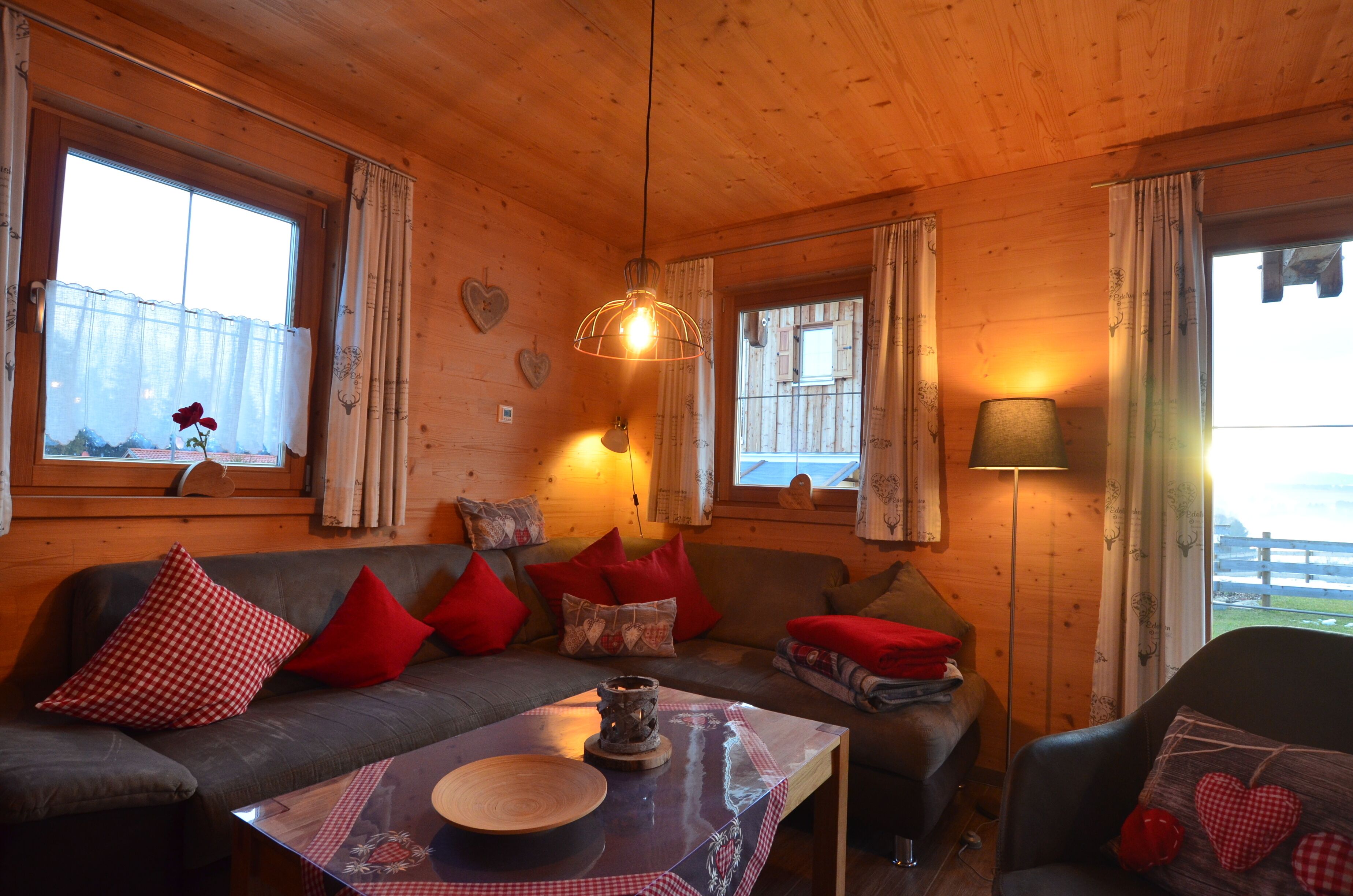 Interior acollidor d'una cabana amb parets de fusta, un sofà amb coixins vermells i estampats, una taula amb un bol i una làmpada penjant.