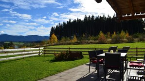 A patio with outdoor seating, a wooden fence, and a view of a forest and mountains.