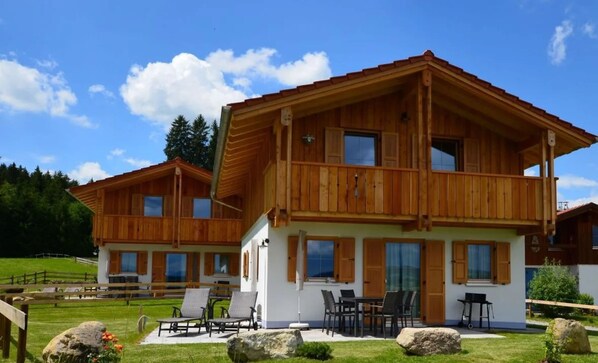 A wooden chalet with a balcony and a patio area with outdoor furniture.