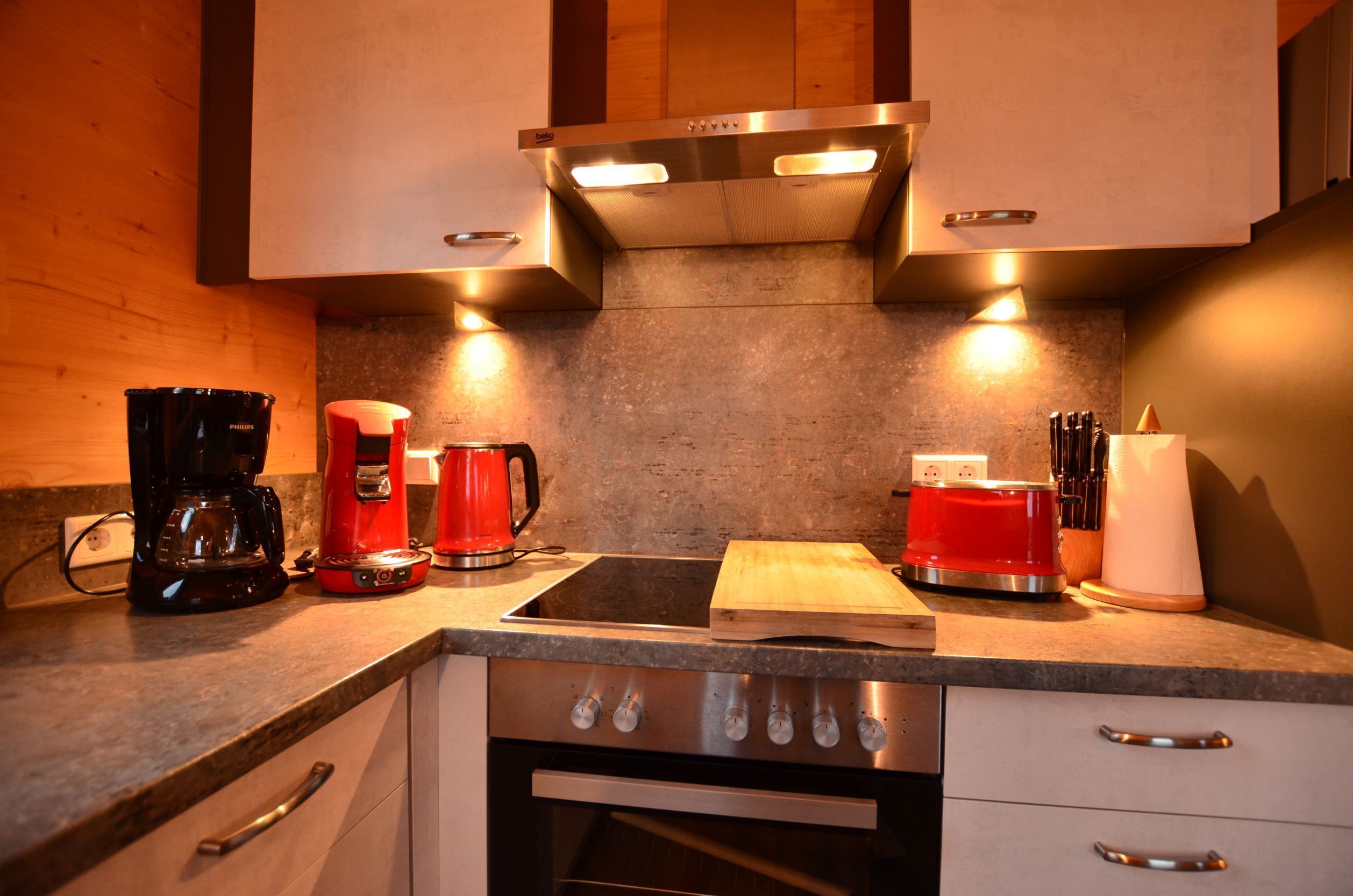 A modern kitchen with a built-in oven, a coffee maker, a toaster, and a knife block.