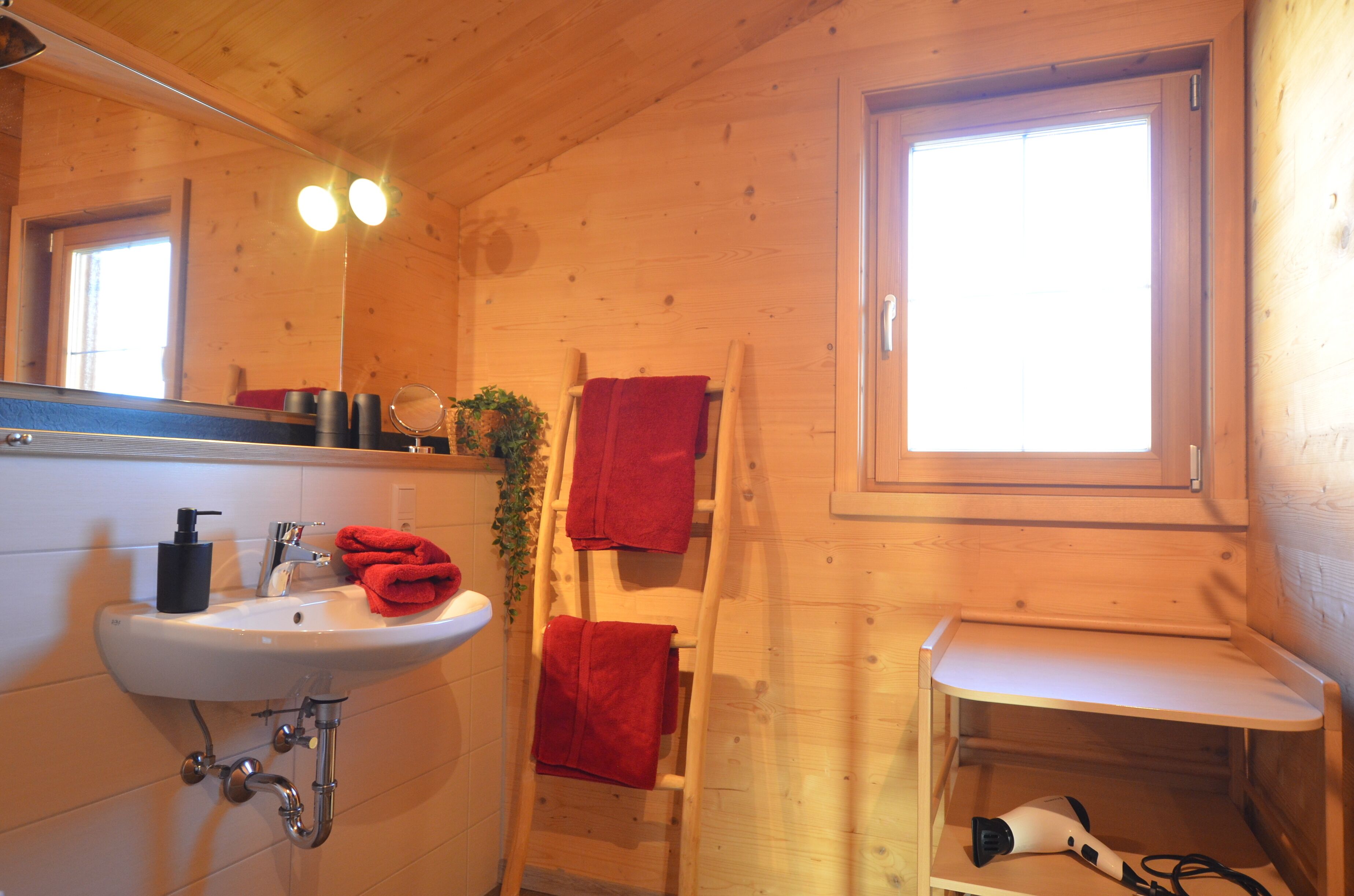 Une salle de bain rustique, aménagée dans une cabane en bois, avec un lavabo, un miroir et une fenêtre.