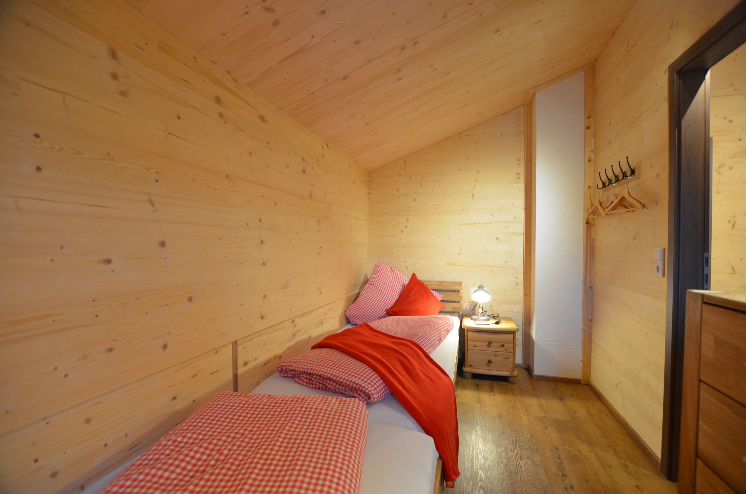 Una habitación de cabaña de madera con una cama individual, una mesita de noche y un armario de madera.