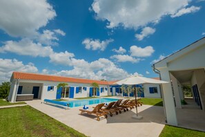 A modern building with a swimming pool, lounge chairs, and a covered patio area.